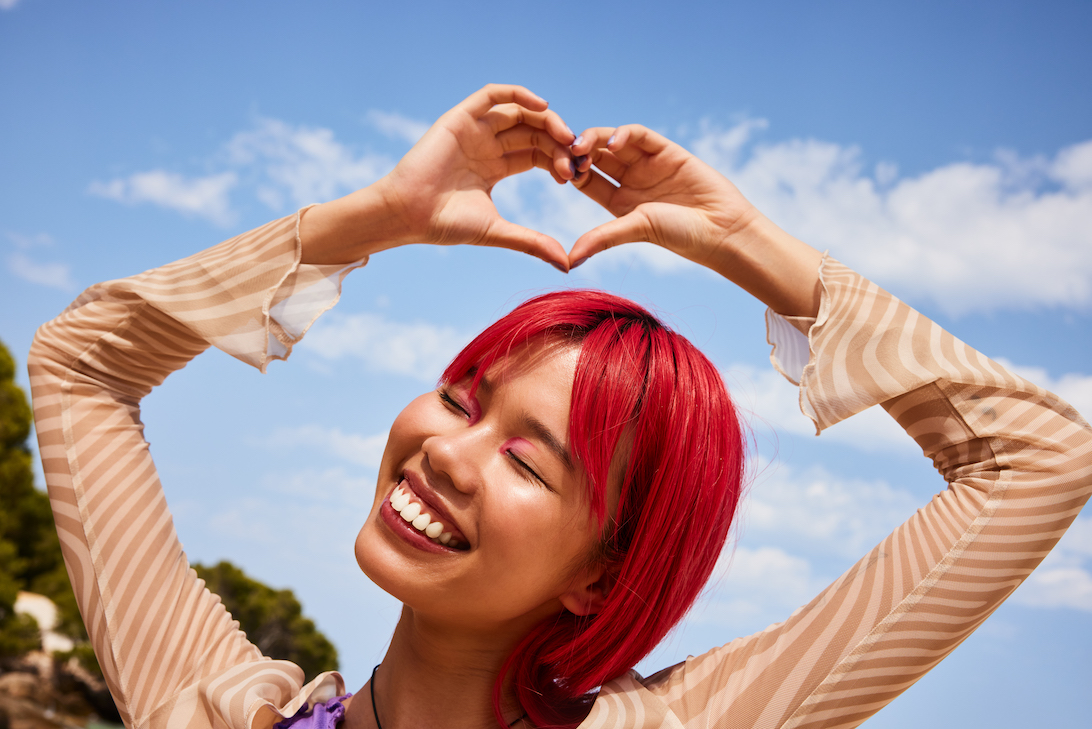 Model with red hair making a heart shape for the essence campaign